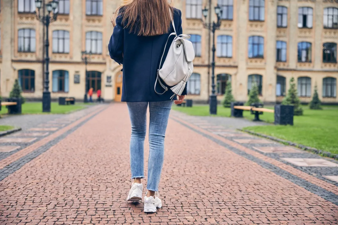 Studentka z plecakiem idzie alejką w stronę budynku uczelni