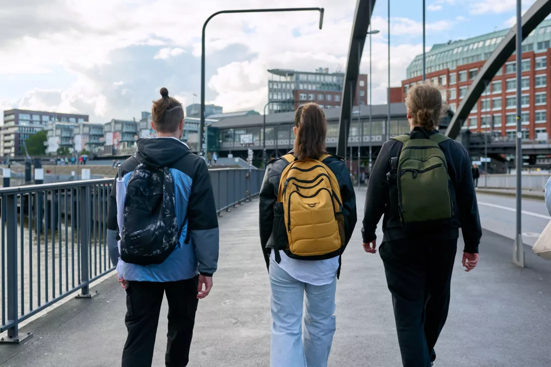 Troje studentow z plecakami idzie razem ulica miasta