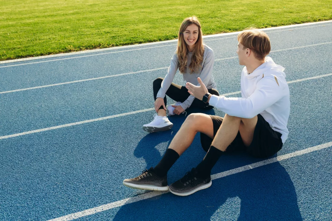 Dwoje studentów w strojach sportowych rozmawia na bieżni stadionu