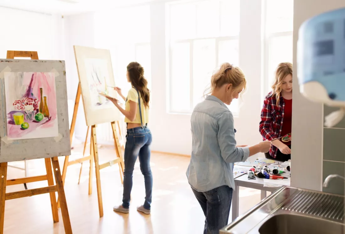 Studentki malują martwą naturę przy sztalugach w jasnej pracowni artystycznej