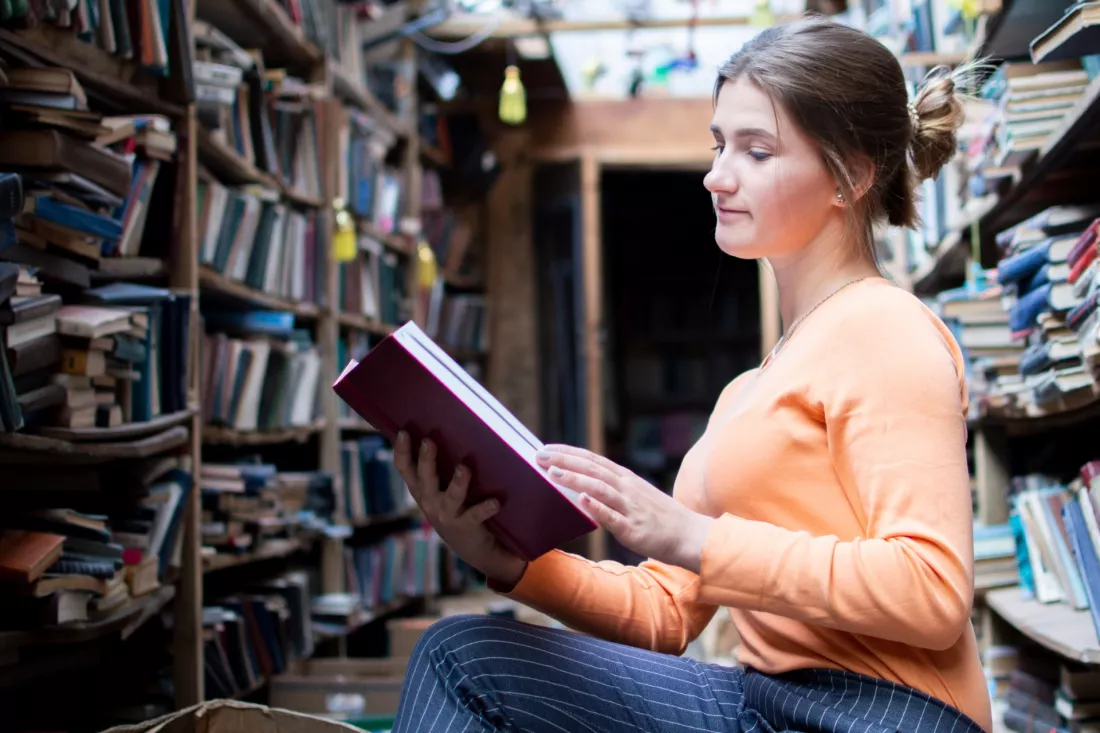 Studentka czyta książkę między regałami w bibliotece